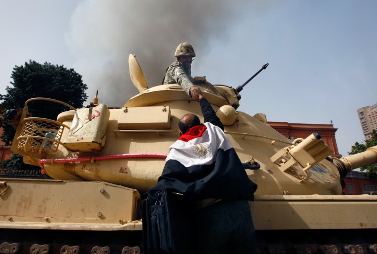 Image: A protester draped in an Egyptian flag climbs atop an army tank to shake hands with a soldier in Cairo