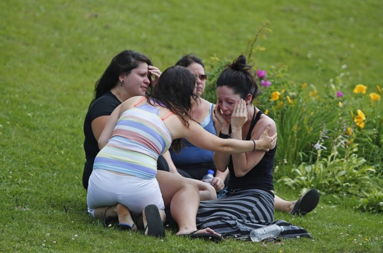Image: A woman comforts her friend while they sit on the grass at the Polyvalente Montignac, the school sheltering the people who were forced to leave their houses after the explosion, in Lac Megantic