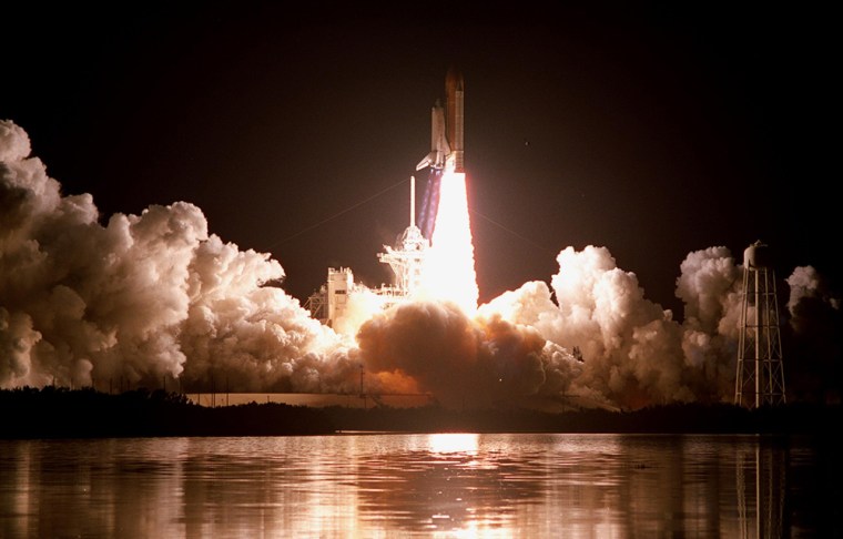 Like a rising sun, space shuttle Discovery rockets into the night sky on the STS-103 mission on Dec. 19, 1999 at 7:50 p.m. EST. The brilliant light creates a reflection of the launch in the water nearby. STS-103 was a servicing mission for the Hubble Space Telescope. It was the 27th flight of Discovery and the 96th mission for the space shuttle program.