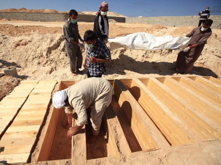 Image: A Libyan volunteer prepares a grave for the body of one of the six soldiers loyal to Gaddafi that were left behind, at a cemetery in Misrata