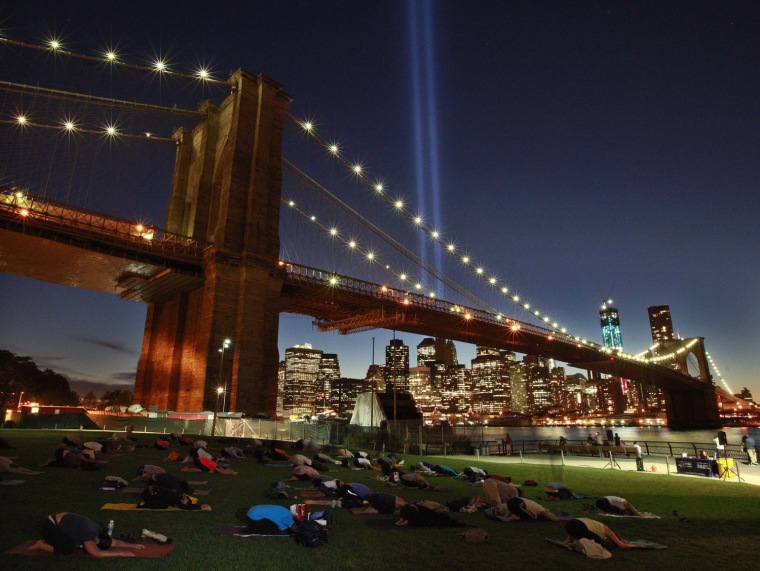 Image: People take part in a sunset yoga session as the Tribute in Light shines over the Brooklyn Bridge on the East River on the 11-year anniversary of the 9/11 attacks in New York