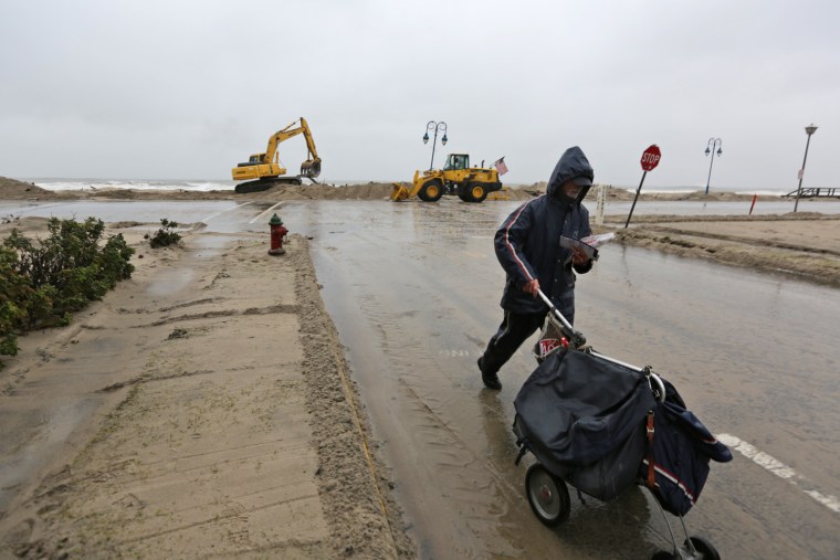 Image: Postal carrier Kenneth Henn delivers mail to a residence along Ocean Ave. at 15th Street in the evacuated section of Belmar, N.J., Nov. 7, 2012, as earth moving machines pile sand along Ocean Ave.