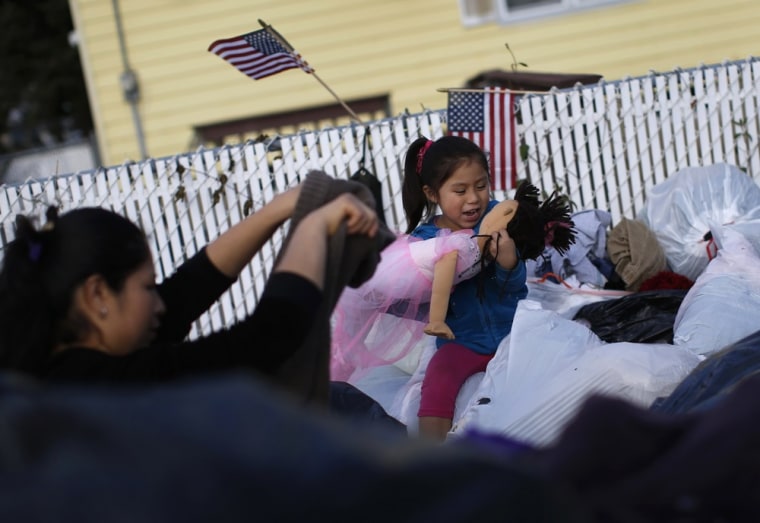 Image: A young girl rejoices as she finds a doll, while she and her mother search through piles of clothes and other items donated for victims of Hurricane Sandy, on a sidewalk on the South side of Staten Island in New York City