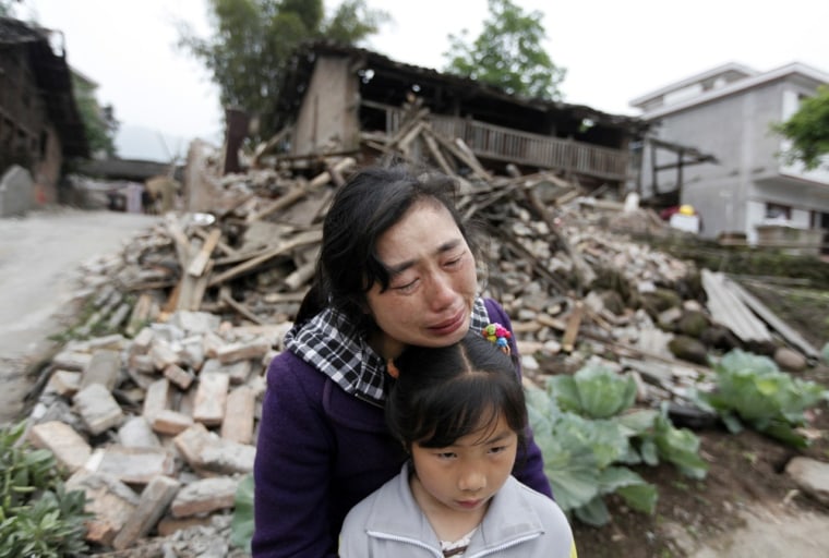 Image: A woman, holding her daughter, cries in front of her damaged house after a strong 6.6 magnitude earthquake at Longmen village, Lushan county