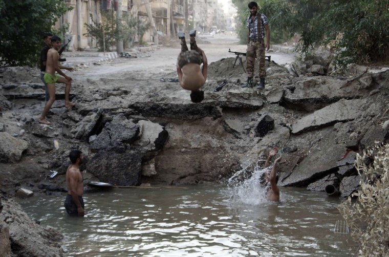Image: A Free Syrian Army fighter dives into a crater filled with water in Deir al-Zor