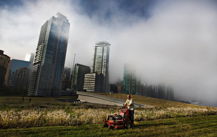 Image: Morning fog drifts across downtown as landscaper Graham Reid cuts the grass on top of the Vancouver Convention Centre's living roof in Vancouver