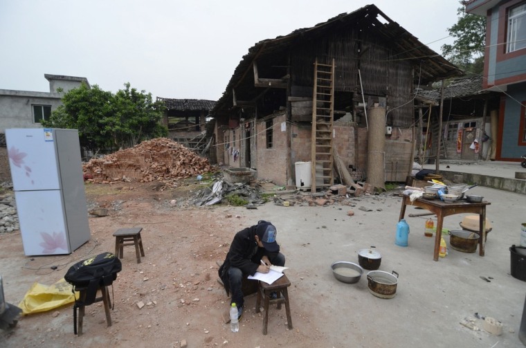 Image: A student does his homework in front of damaged houses on the second day after an earthquake hit Longmen township of Lushan county