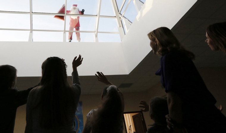 Image: Trifonov, a member of the \"Rescuer\" state regional service, dressed as Santa Claus, looks through a roof window as he congratulates employees of the Russian Emergencies Ministry and their children ahead of the Christmas celebrations in Krasnoyarsk