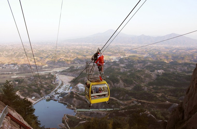 Image: A staff of Shiniuzhai scenic zone dressed as Santa Claus stands on top of a cable car to send gifts to visitors, in Pingjiang