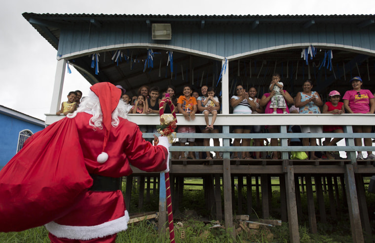 Image: A member of the Amigos do Papai Noel dressed as Santa Claus talks to children before giving out gifts to them at the community Sao Jose in Careiro da Varzea