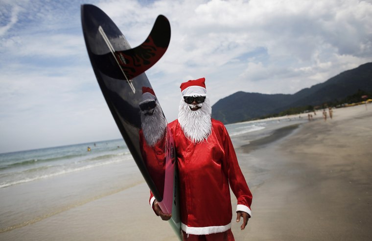 Image: Carlos Bahia, dressed as Santa Claus, poses with his board at the Maresias beach, in the state of Sao Paulo