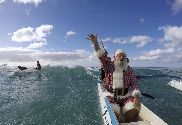 Image: Donald Boyce, dressed up like Santa Claus, waves to surfers as he goes outrigger canoe surfing off Waikiki beach in Honolulu