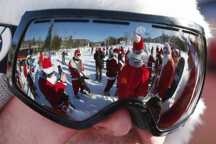 Image: Skiers and snowboarders dressed as Santa Claus are reflected in a skier's goggles before participating in a charity run down a slope at Sunday River Ski Resort in Newry
