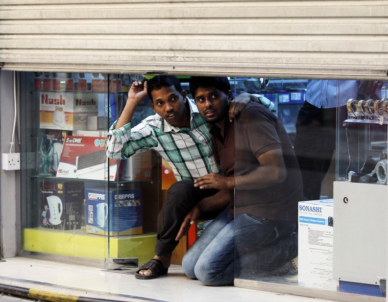 Image: Shop owners look out from under the shutters of their shop during an anti-government protest in the capital Manama