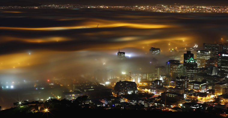 Image: Seasonal fog is illuminated by the lights of  Cape Town harbour as the city prepares for the start of the southern hemisphere winter