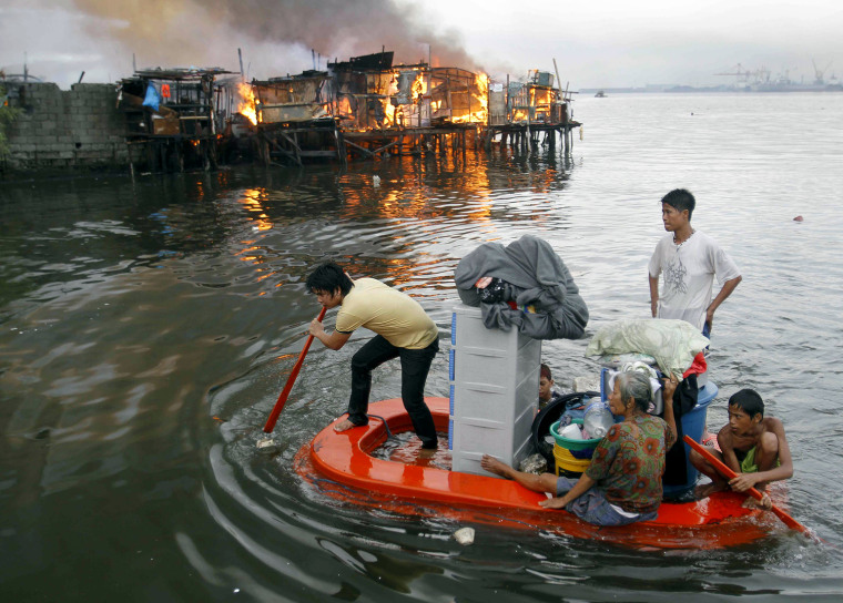 Image: Residents paddle their makeshift boat to safety as fire engulfs houses at a slum community in Manila