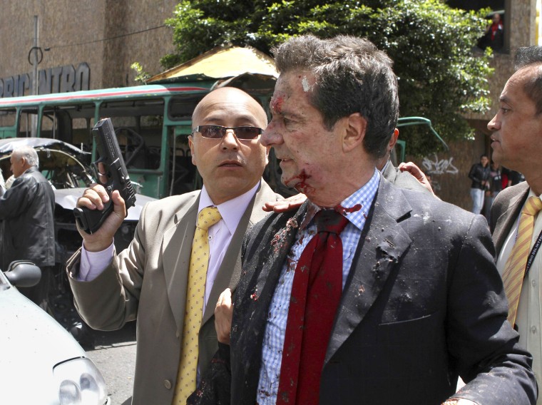 Image: Former Colombian Interior Minister Fernando Londono, who is injured, walks as he is guarded by a bodyguard after an explosion in a central avenue in Bogota
