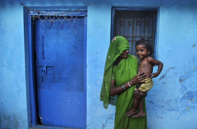 Image: An Indian woman holds her child outside her house in Allahabad