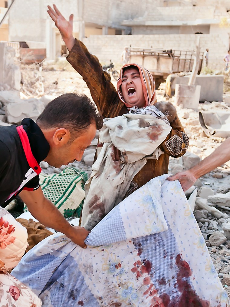 Image: A Syrian woman holds her dead baby as she screams upon seeing her husband's body