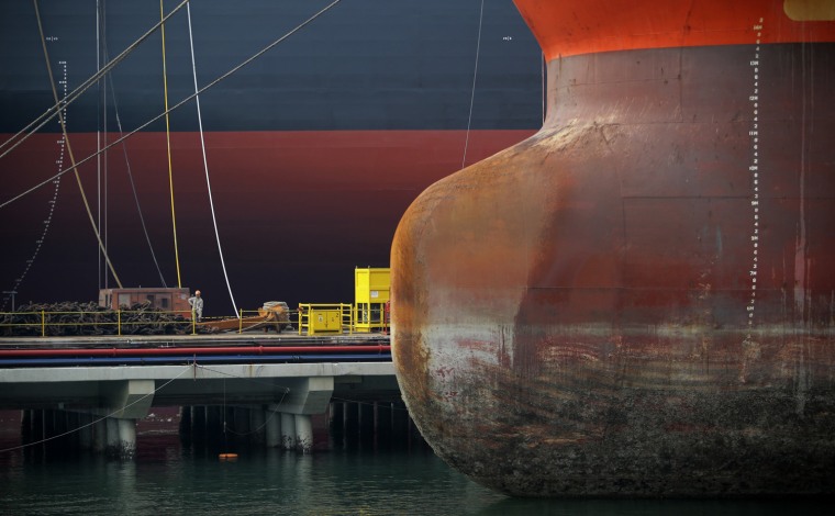 Image: A worker is dwarfed by vessels berthed at a pier in Keppel Shipyard in Singapore