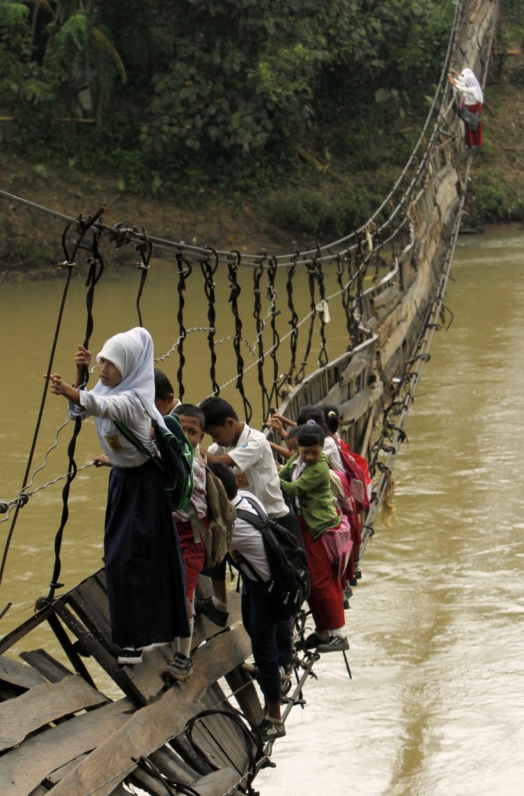 Image: Students hold on to the side steel bars of a collapsed bridge as they cross a river to get to school at Sanghiang Tanjung village in Lebak regency