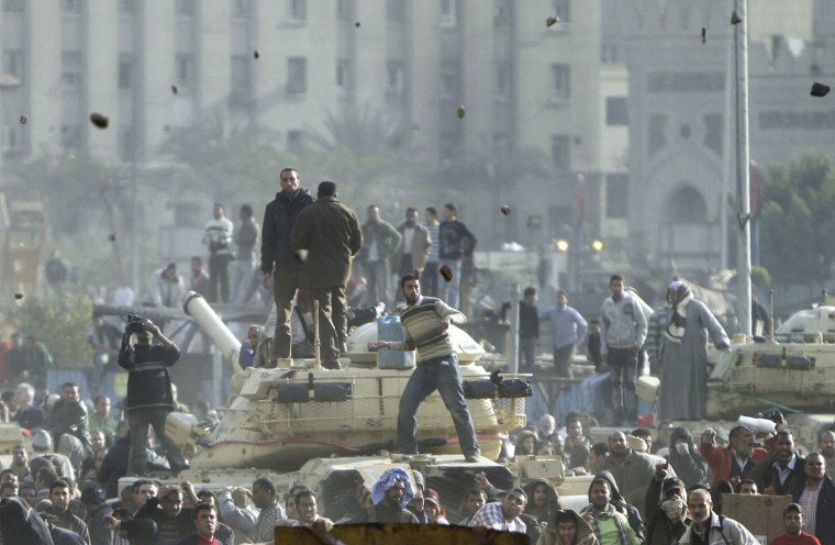 Image: Stones fly through the air as supporters of President Hosni Mubarak, foreground , fight with anti-Mubarak protesters, rear, standing on army tanks