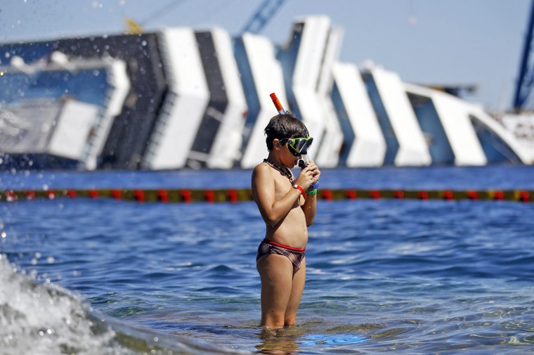 Image: A boy prepares to snorkel in front of the wreckage of capsized cruise liner Costa Concordia, near the harbour of Giglio Porto