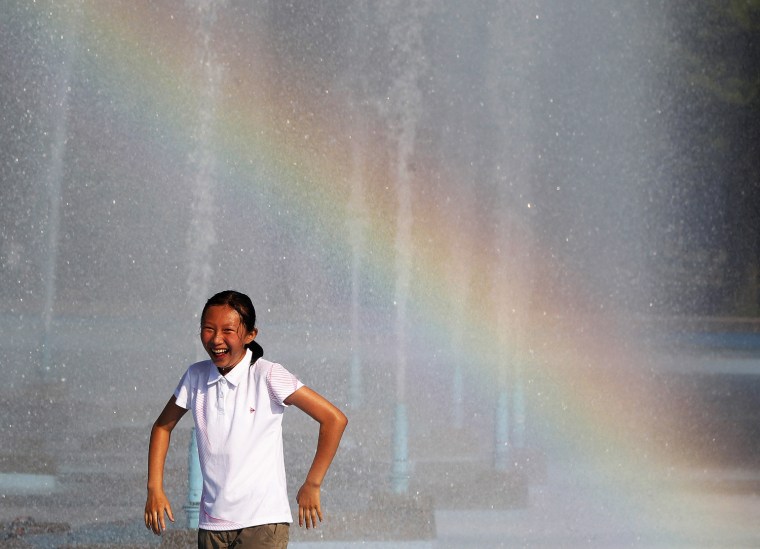 Image: A girl cools off in the Unisphere fountain at the Flushing Meadows-Corona Park as a rainbow streaks across the water in the Queens borough of New York