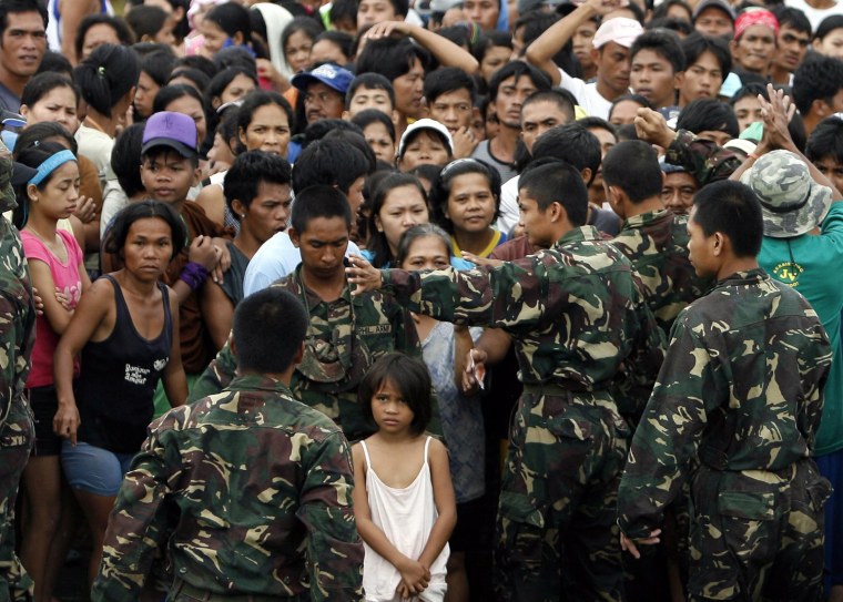 Image: Filipino flood victims wait along a military cordon during relief distribution in devastated area caused by floodings in the town of Taytay