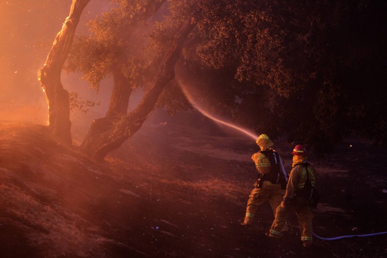 Image: Firefighters spray water near a burning house in the Twin Pines Road area at the Silver Fire near Banning, California.