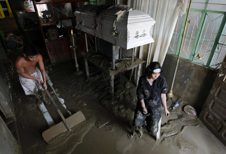 Image: Filipino Jenelyn Tabigni (R) sits beside the coffin of her mother, Daisy, as her husband push mud inside their house during a wake in the town of Rosales