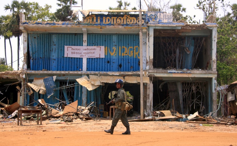 A Sri Lankan government soldier walks past a destoyed building in the town of Putumatalan located near the 'No Fire Zone' in northern Sri Lanka