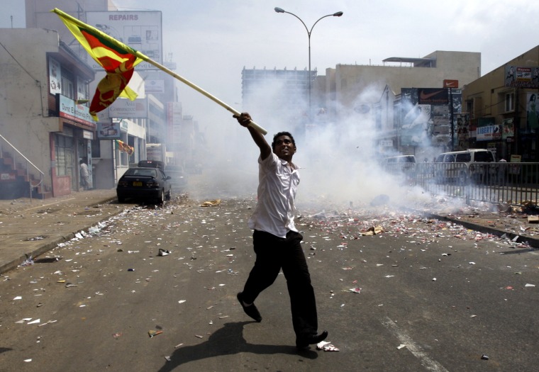 Image: A Sri Lankan man runs while waving his national flag as fireworks explode behind him during celebrations on the streets in central Colombo