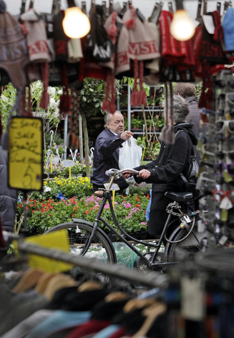In this photo taken on April 17, 2009, a vendor at a stand selling flowers and plants hands over a bag to a customer at Albert Cuyp market in Amsterdam, Netherlands. The inner city of the Dutch capital is a compact warren of heritage buildings, of museums both grand and odd, of hidden gardens and outdoor markets, all within easy reach by any mode of transport except the unwelcome car. No longer the bargain city of Europe, Amsterdam is still a city of wonders that can be had for a discount, and sometimes for free. (AP Photo/Peter Dejong)