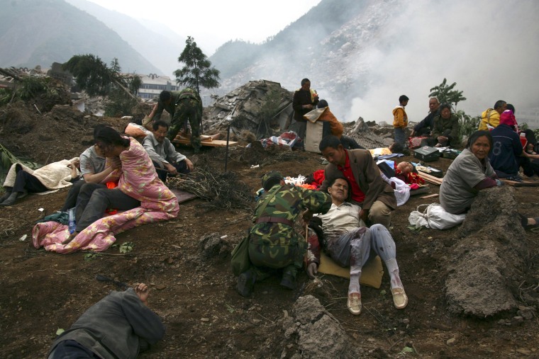Injured victims from the earthquake on Monday sit on the rubble in Beichuan