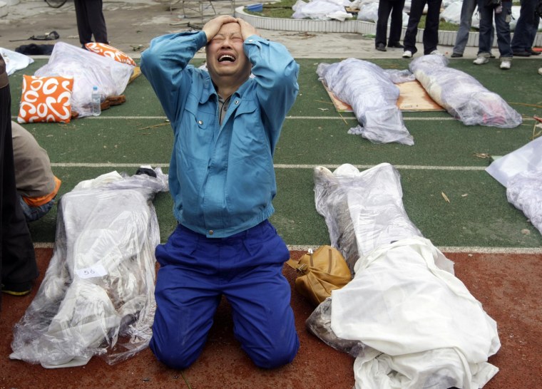 A father cries next to the recovered body of his son that is laid out with other bodies at the playground of a school at the earthquake-hit Hanwang Town