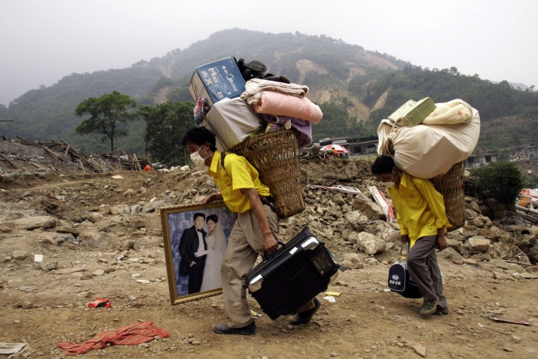 Two residents, one carrying a wedding picture of their relatives and and other belongings, evacuate the disaster area in Beichuan county, southwest China's Sichuan province, China, Saturday, May 17, 2008. The man in the wedding image was killed in Monday's earthquake.  Thousands of Chinese earthquake victims fled areas near the epicenter Saturday, fearful of floods from a river blocked by landslides.  (AP Photo/Vincent Yu)