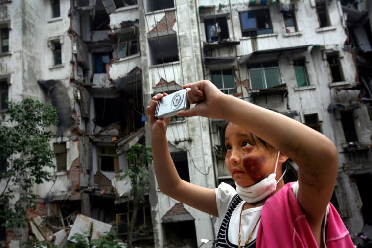 Nine-year-old Xia Xueyin, her face badly bruised from a fall during last week's earthquake, takes photos of her family's damaged home in Hanwang town of China's southwest Sichuan province Thursday, May 22, 2008. The girl's parents said that they brought her back to her home to see the damage and to look for her belongings to help her cope with the trauma of having experienced the May 12 earthquake. (AP Photo/David Guttenfelder)
