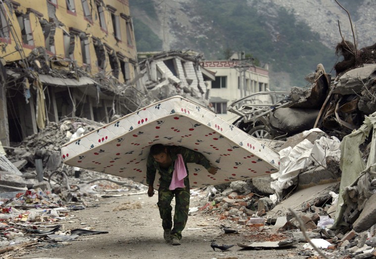 A Chinese man carries a mattress he removed from a destroyed apartment in Yingxiu in Wenchuan County of southwest China's Sichuan province Tuesday, May 27, 2008.  The number of deaths from the quake has climbed further toward an expected toll of 80,000 or more. The Cabinet said Tuesday that 67,183 people were confirmed killed _ up by about 2,000 from a day earlier _ and 20,790 were sill missing.(AP Photo/David Guttenfelder)
