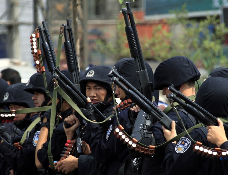 Image: Armed Chinese policemen march towards a group of local women during a confrontation along a street in the city of Urumqi