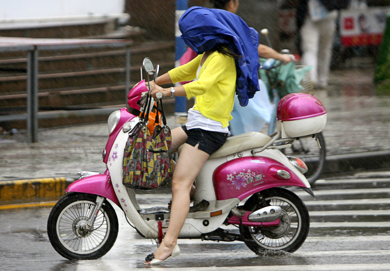 Image: A motorist with her head covered struggles to ride a scooter amidst strong winds brought about by typhoon Morakot in Nanjing