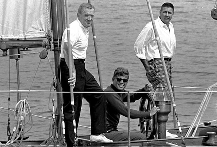 John F. Kennedy takes the wheel of the Coast Guard yawl Manitou for a cruise along Down East Maine, Aug. 11, 1962, as Sen. Benjamin Smith, who took the senate seat vacated by Kennedy, stands at right. (AP Photo)