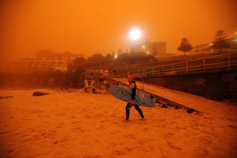 Image: A surfer heads for the water as a dust storm blankets Bondi Beach in Sydney