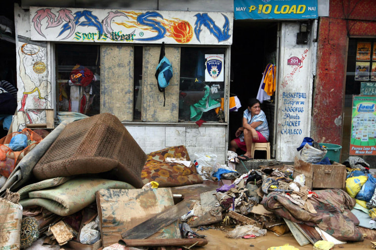 Image: A Filipino looks out from a damaged tailoring shop amidst debris washed to the streets by floods in Marikina City