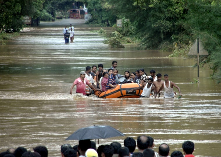 Image: People use a rescue raft as they wade through floodwaters in Kudal village