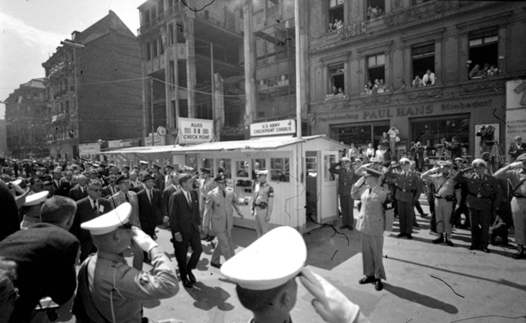 Walking past a cordon of saluting servicemen and the sentry post of \"Checkpoint Charlie,\" President Kennedy arrives June 26, 1963, at the West Berlin area near the Berlin Wall where less than two years ago Russian and U.S. tanks faced each other muzzle to muzzle.  Escorting the President is Brig. Gen. Frederick O. Hartell, right, Commander of the U.S. brigade in Berlin.  Partly obscured by Kennedy is West Berlin Mayor Willy Brandt.  (AP Photo)