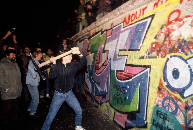 A man attacks the Berlin Wall with a pickaxe on the night of November 9th, 1989