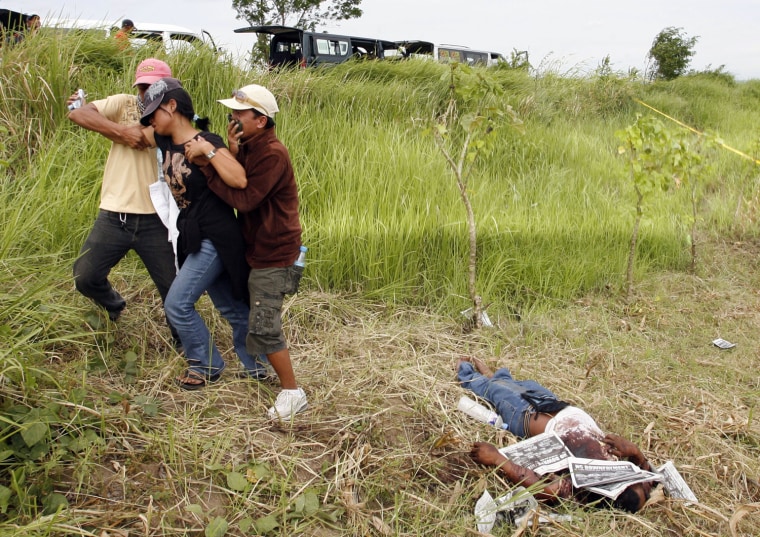 Image: Wife of a local reporter is led away from the scene of a massacre on the outskirts of Ampatuan