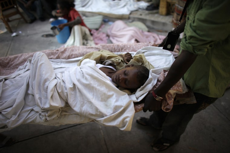 Image: Boy is carried away in a stretcher at a makeshift hospital in the streets of Port-au-Prince