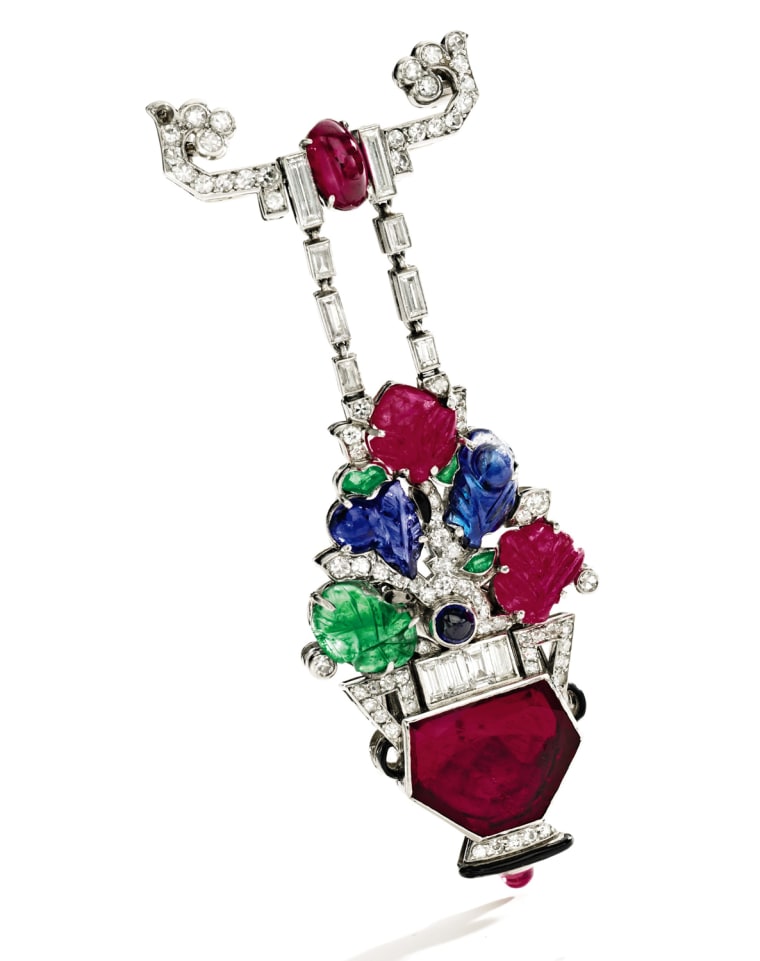 Platinum, Ruby, Sapphire, Emerald and Diamond Pendant-Watch, Mauboussin, France, Circa 1930
The jardinière suspended from a stylized bar pin, set with a table-cut ruby, cabochon and carved rubies, cabochon and carved sapphires, carved and buff top caliber-cut emeralds, and baguette and single-cut diamonds weighing approximately 2.00 carats, the reverse showing an oval dial with Arabic numerals, manual movement, signed Mauboussin, France
Est. $30/50,000